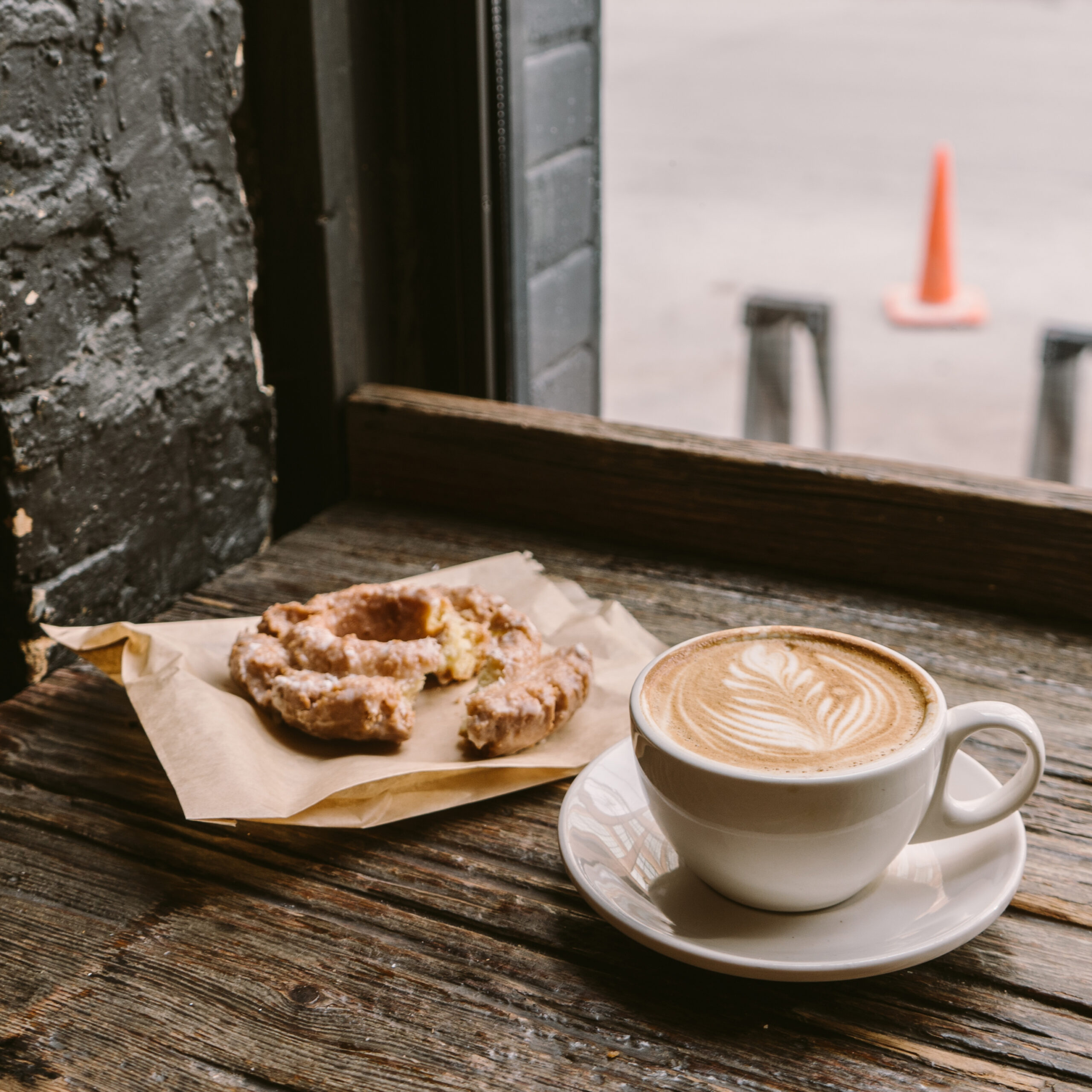 A cup of coffee next to a cookie put on the windowsill