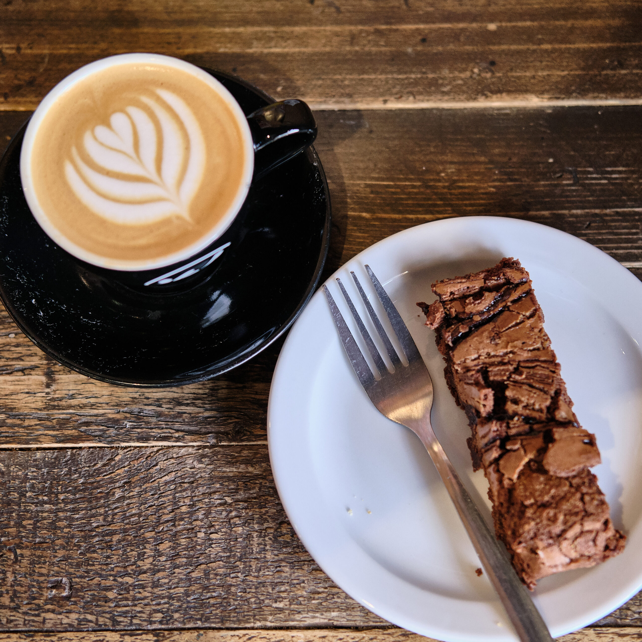 A high angle shot of a cup of coffee and plate of chocolate cake on a wooden table